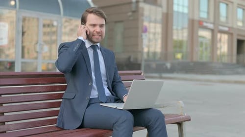 Man Uses Laptop and Cellphone on City Bench