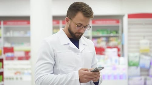 Junger kaukasischer männlicher Apotheker in weißer medizinischer Uniform mit Smartphen