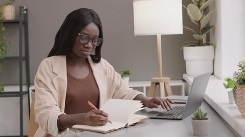 Empresária africana usando laptop e escrevendo no bloco de notas