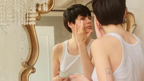 Beautiful Woman Applying Face Cream in Mirror