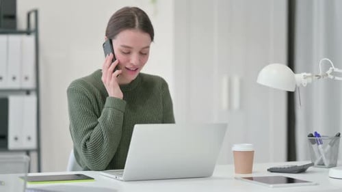 Young Woman Talking on Phone While Working on Laptop