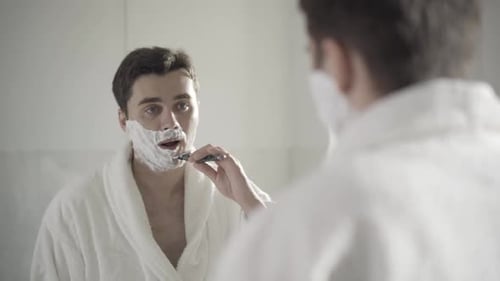 Reflexão de um lindo homem moreno se barbeando com navalha no banheiro