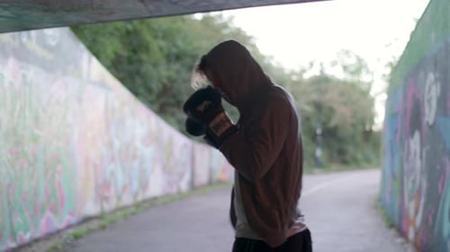 Medium Shot of Young Active Man Boxing In Underpass, Silhouetted By Light