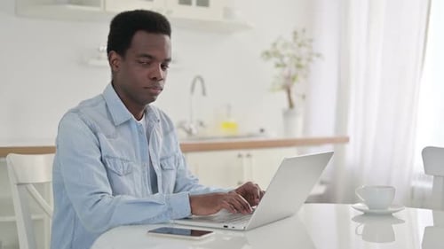 Young Adult Using Laptop in Kitchen, Smiling