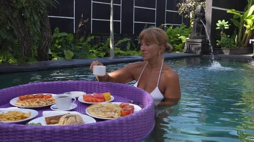A Middleaged Woman in a Swimming Pool Having a Floating Breakfast