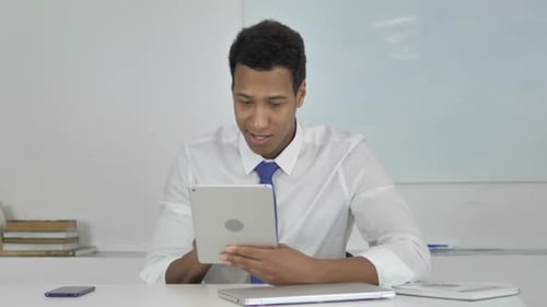 Young Adult Male Celebrates Success on Tablet in Office