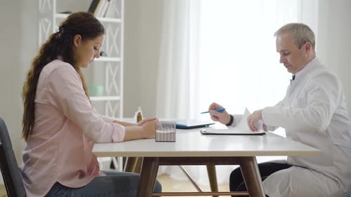 Side View of Young Caucasian Woman Sitting in Hospital with Doctor and Listening To Consultation
