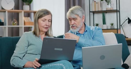 Casal sênior descansando em um sofá confortável com laptops pessoais