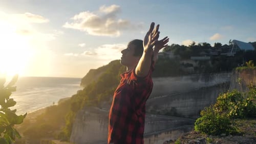 Young Man Traveler Raising His Hands High on Top of the Mountain Above Beautiful Landscape on Golden