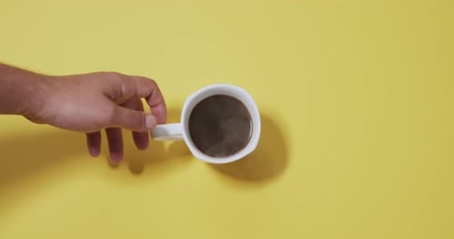 Hand Reaching for Steaming Coffee Mug on Yellow