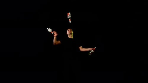 Young Man Juggling Bottles with Skill on Black Background