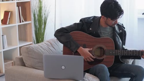 Young Man Playing Guitar While Looking at Laptop