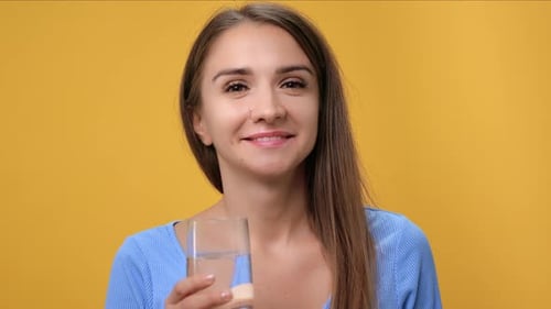 Nahaufnahmeporträt einer glücklichen jungen Frau, die sauberes reines Wasserglas trinkt und isoliert auf Orange posiert