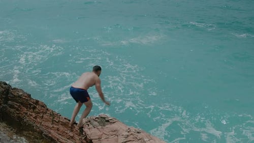 Junger Mann springt in Montenegro von einem Stein in die azurblaue Adria mit Wellen