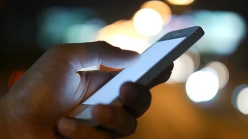 Hand Using Cellphone in the City at Night