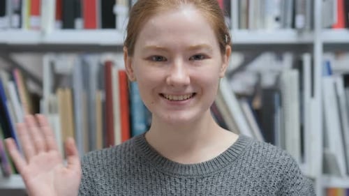 Hello by Junge Frau sitzt zu Hause auf Stuhl und winkt mit der Hand