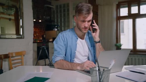 Man Working on Laptop and Talking on Phone