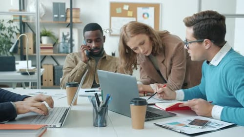 Gruppe von Büroangestellten, die mit Routinetätigkeiten beschäftigt sind und Laptops verwenden, auf Mobiltelefonen