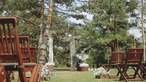 Weeding Arch Decorated with Pastel Faded Flowers and Wooden Chairs in the Park Slow Motion Shot