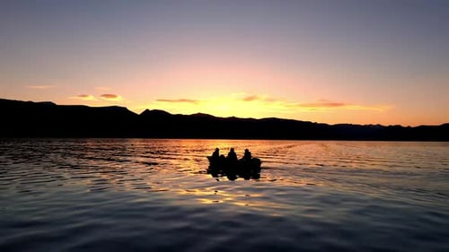 4 people fishing in a boat floating on a lake at sunset