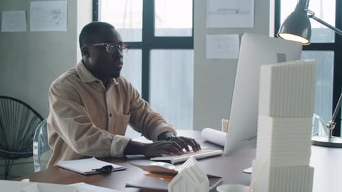 Junger afroamerikanischer Architekt arbeitet am Computer und macht sich Notizen
