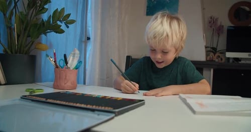 Glückliches lächelndes Kind, Junge, der am Abend auf Papier mit Farbstift zeichnet