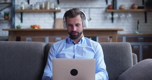 Sitting on Couch Using Laptop Notebook Looking at Screen Typing Message Focused Man in Headphones