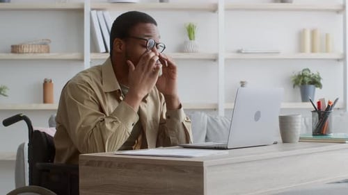 Tired Handicapped Man In Wheelchair At Laptop Rubbing Eyes Indoor