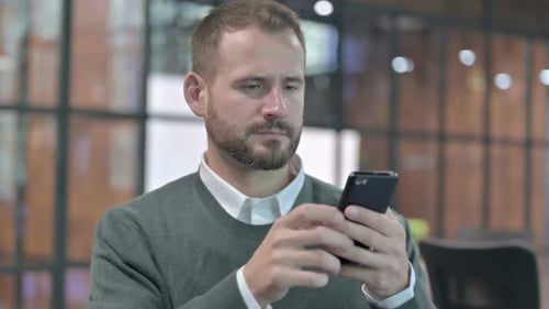 Man Looking at Smartphone, Appears Distressed and Upset