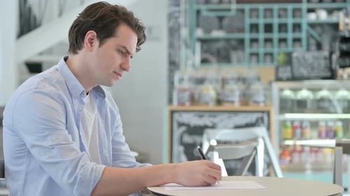 Frustrated Man Writing at Cafe Table