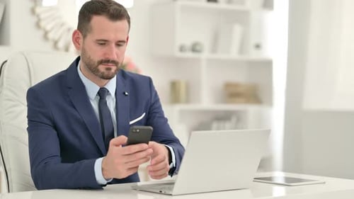 Professional Businessman Using Smartphone and Laptop in Office