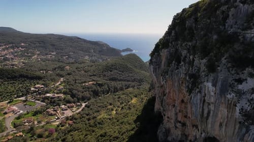Forward droneshot along steep cliff of foresty green mountain in Greece. Revealing clear blue sky an