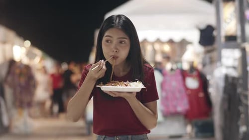 Asian young women travel in Thailand walking and eating Pad Thai at The Khao San Road.