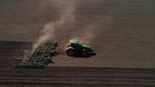 Tractor with harrow system plowing ground on cultivated farm field, agriculture.