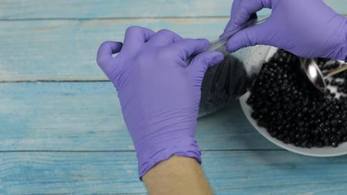 Gloved Hands Scooping Berries into Bowl