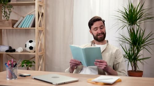 Man Reads Book at Desk Indoors