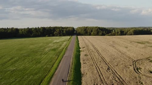 Straight Road in Agriculture Side. Man Rides a Motorcycle on a Sunset Passing in Scene. Aerial View