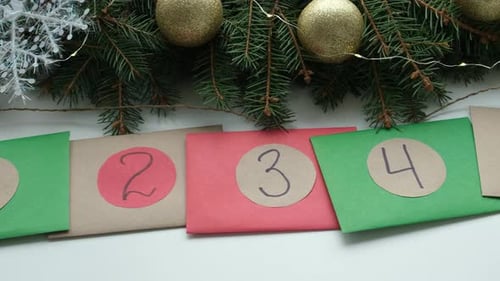 Homemade Christmas Advent Calendar Multicolored Envelopes with Numbers Lie on the Table Near Green