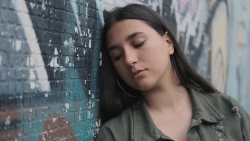 Young Woman Leaning Against Graffiti Brick Wall