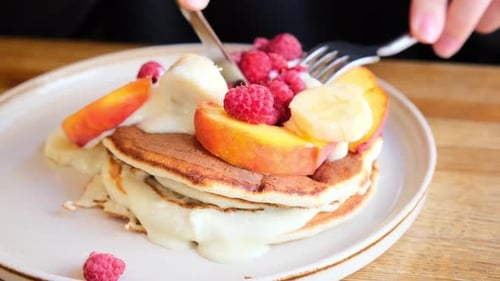 Woman eating pancakes with fruit and cream for breakfast in cafe.