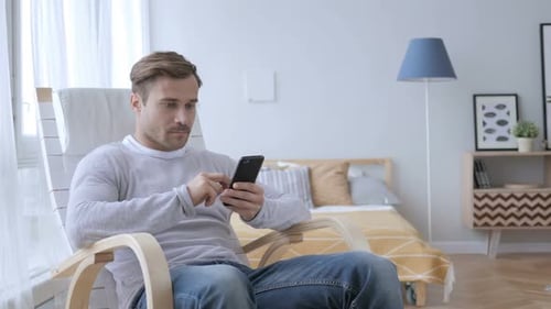 Erwachsener Mann benutzt Smartphone beim Entspannen auf dem Stuhl