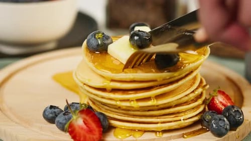Cutting Stack of Pancakes with Berries and Syrup