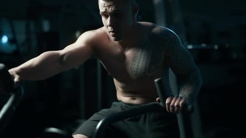 A Handsome Young Muscular Sportsman is Doing Exercise on a Fitness Machine in the Gym