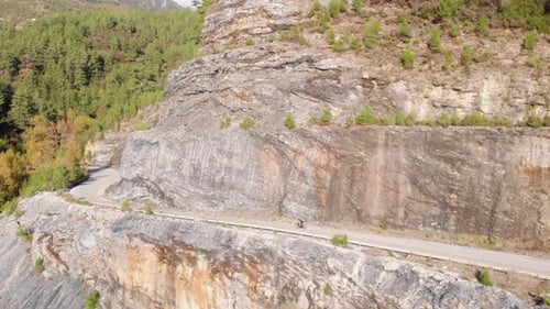Cyclist going down serpentine road in mountain woods.