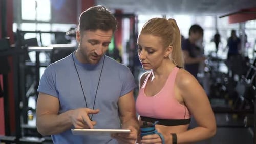 Trainer and His Attractive Female Client Discussing Workout Program in Gym