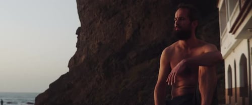 Homem pensativo sentado à beira-mar