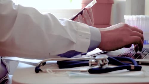 Doctor Works with Blood Sample He is Typing a Report on the Latest Vaccine on a Laptop