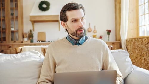 Close Up Portrait of Young Thoughtful Bearded Businessman Working on Laptop at Home Thinking About