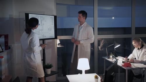 Engineers Discussing Technical Schematics in Office at Night