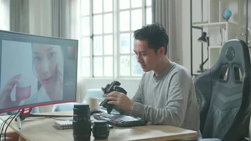 Man Inspecting Camera in Front of Computer Monitor